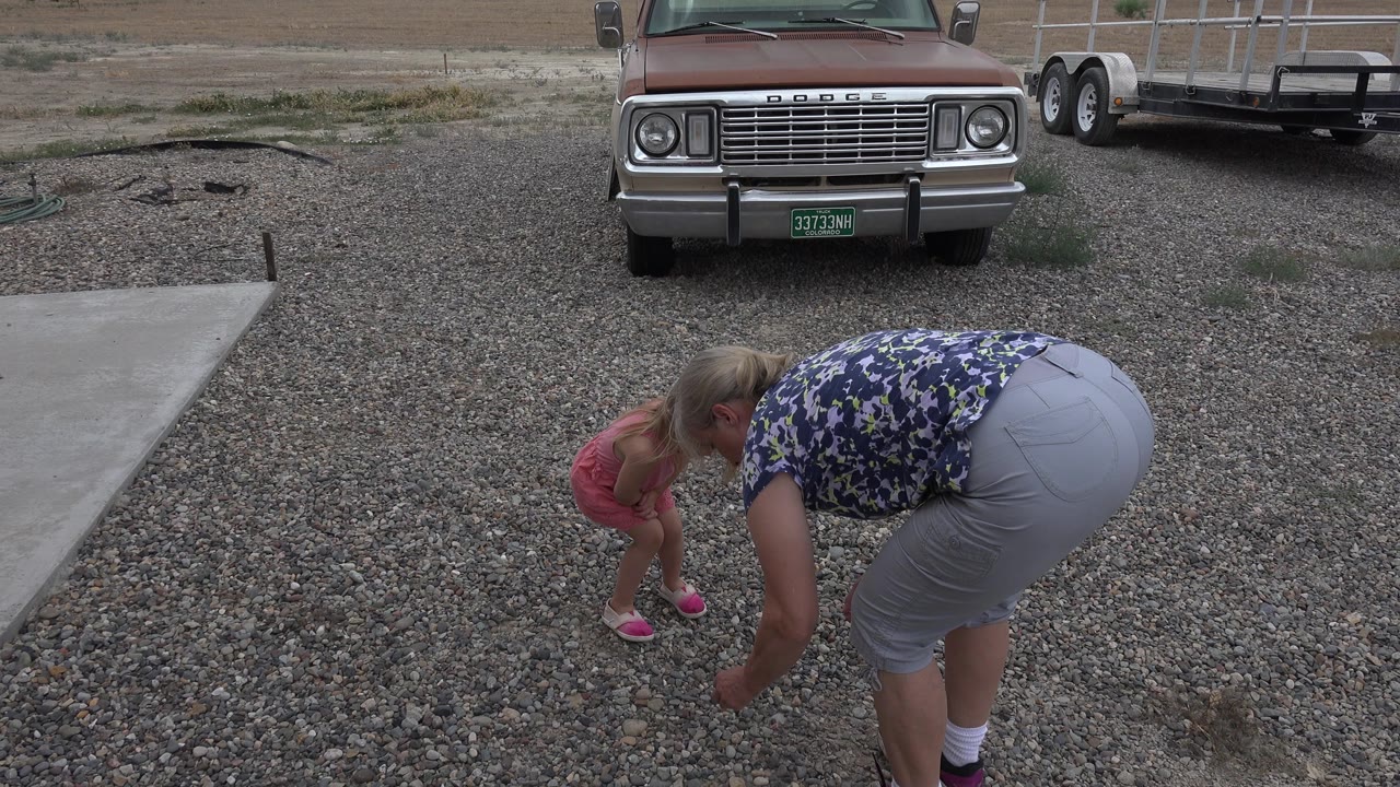 The mother and daughter lean lower over the gravel in Grand Junction, Colorado, while the parked truck grille and trailer stay centered behind them.