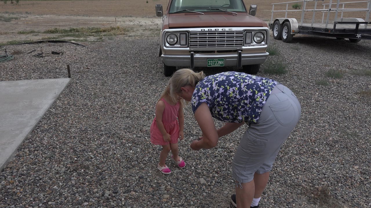 Woman bends beside a young girl standing on the gravel driveway.