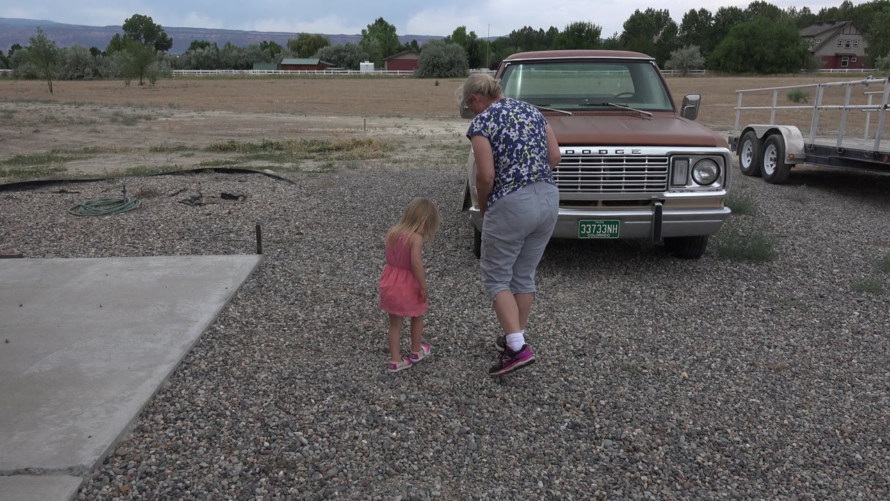 Woman and young girl walking on a gravel driveway near an older truck.