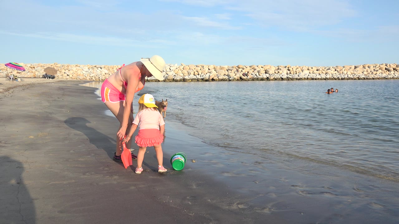 Adult and child with beach toys at the shoreline.