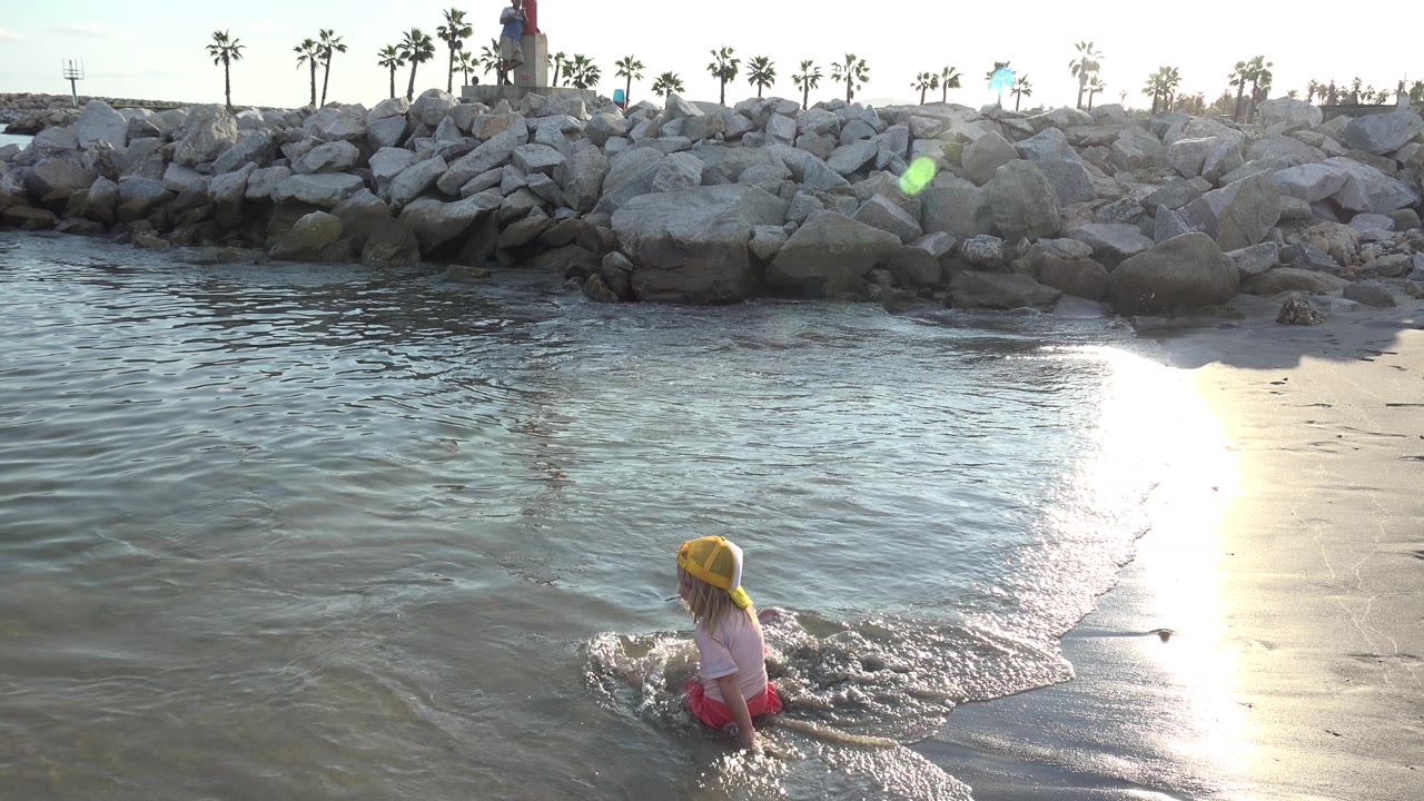 Child wading in shallow water near sunlit wet sand.