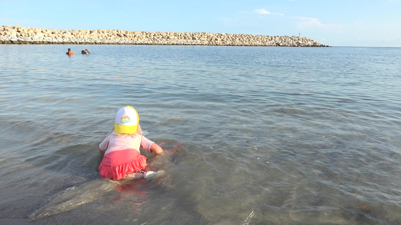 Young girl leaning forward in shallow water with one arm extended toward the surface.