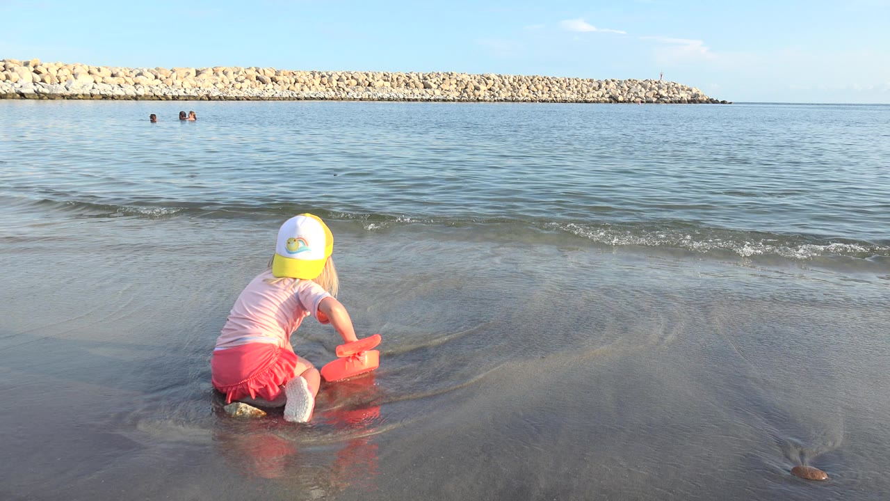 Girl crouched at the shoreline as a wave approaches.