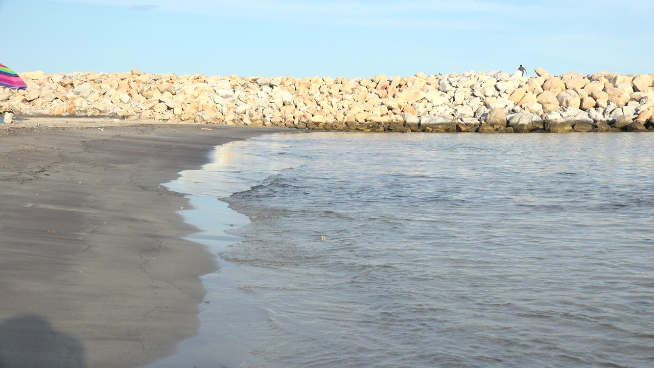 Wet shoreline and shallow water beside a rock barrier with no visible people.
