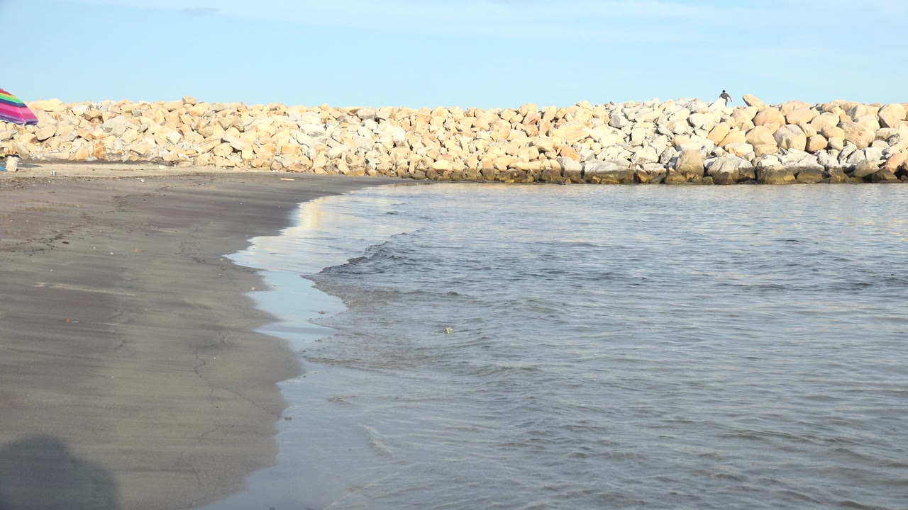 Grand Junction, Colorado waterline spreads across reflective wet sand, with the rock barrier stretching along the horizon and no visible people in the foreground.