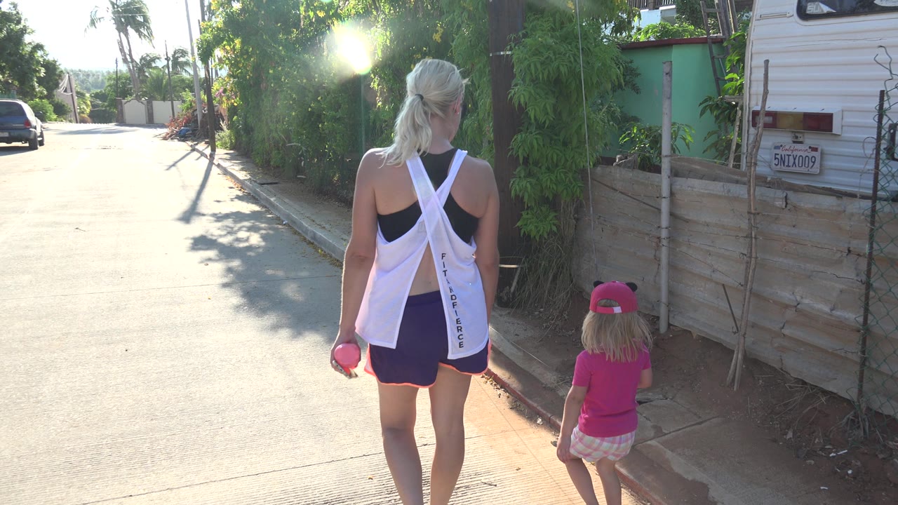 Blonde woman and young girl walking away on a sunny street.
