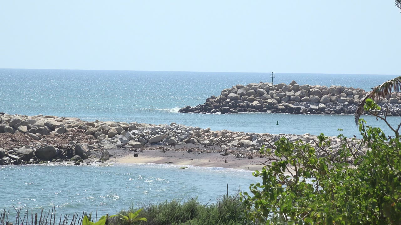 Grand Junction Colorado 2017 frame showing a rock breakwater across the background, calm blue water below it, green foliage at right, and no visible people.