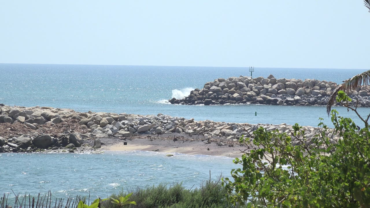 White wave spray hits the rock breakwater under clear sky.