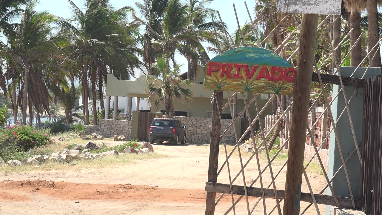 Gated private entrance with palms, a parked car, and a dirt roadside.