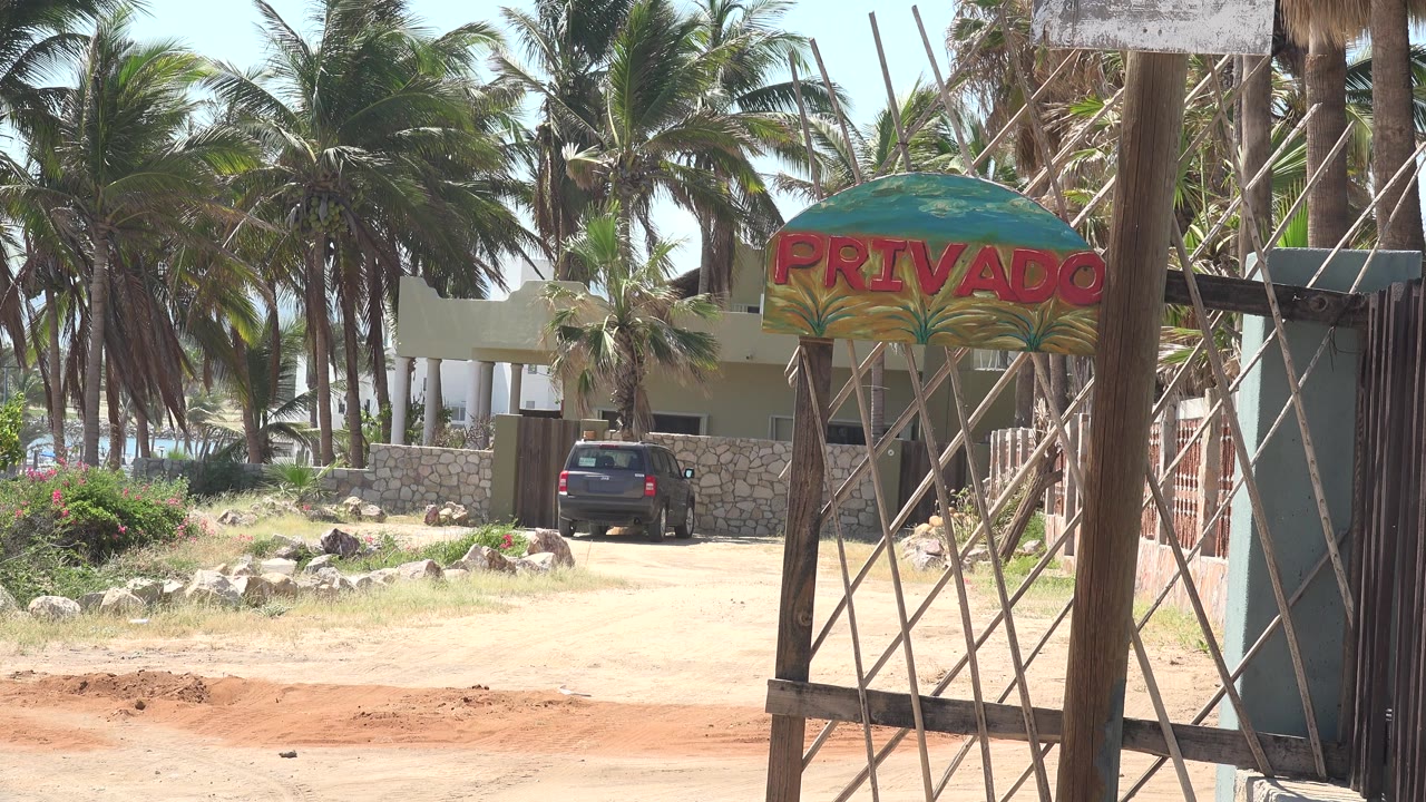 One second in, the Grand Junction, Colorado property entrance remains framed with the painted PRIVADO sign, palm fronds above, a parked car in the driveway, and no visible people.