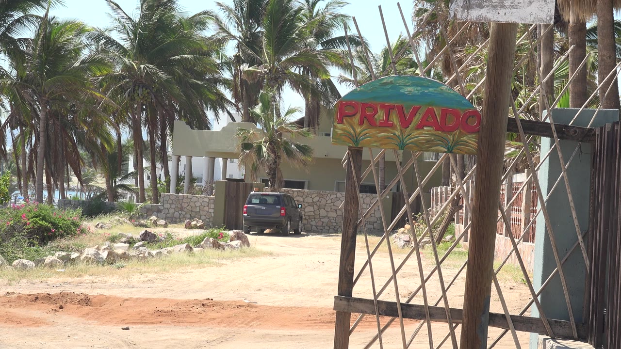 Black car parked near a palm-lined beach entrance with a PRIVADO sign.