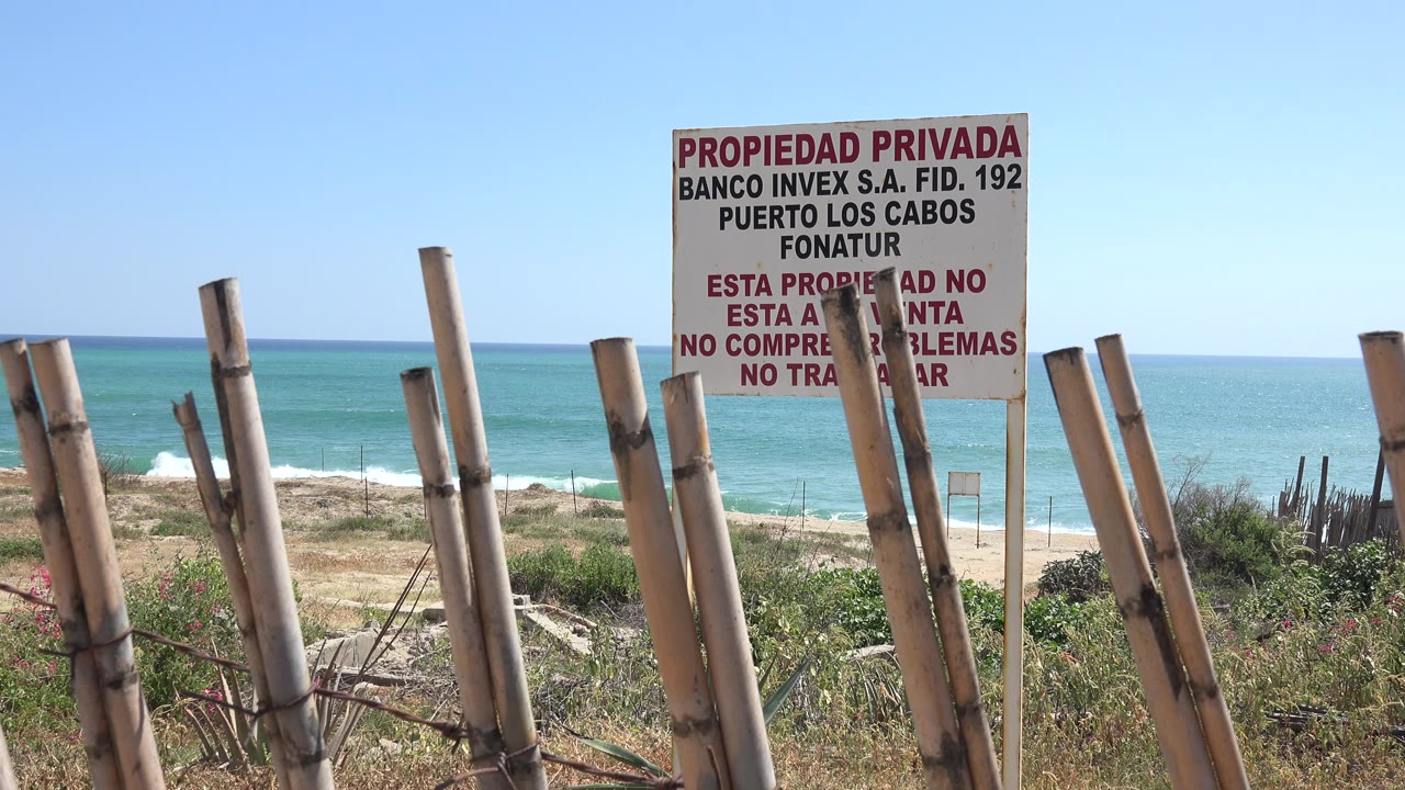 Spanish private property sign behind leaning fence posts with ocean beyond.