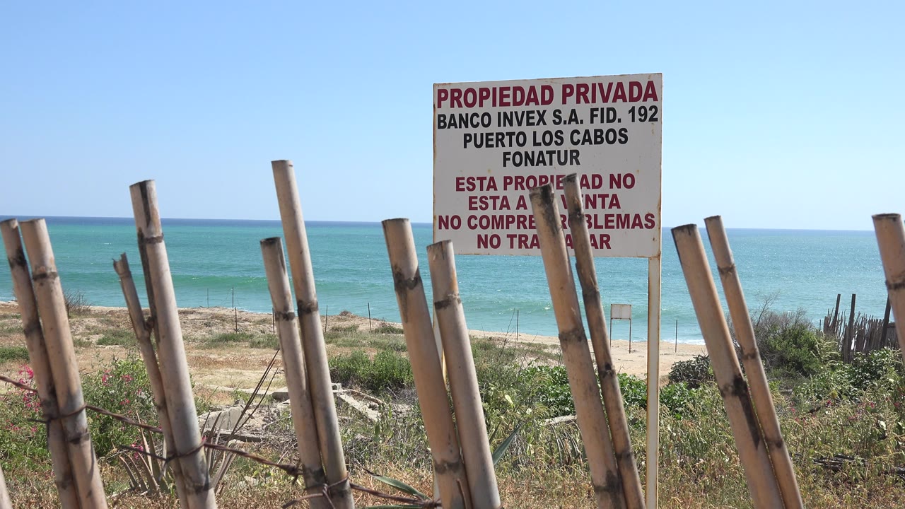 Spanish private property sign behind a bamboo fence above a beach and blue water.