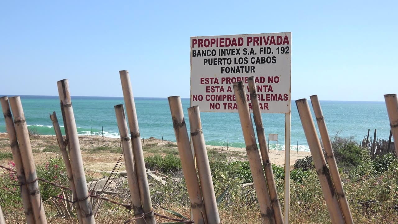 Private property sign above wooden fence posts with blue water and sky behind it.