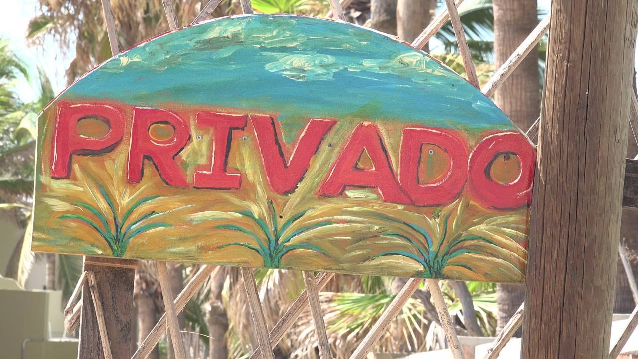 Weathered PRIVADO sign with plants behind it