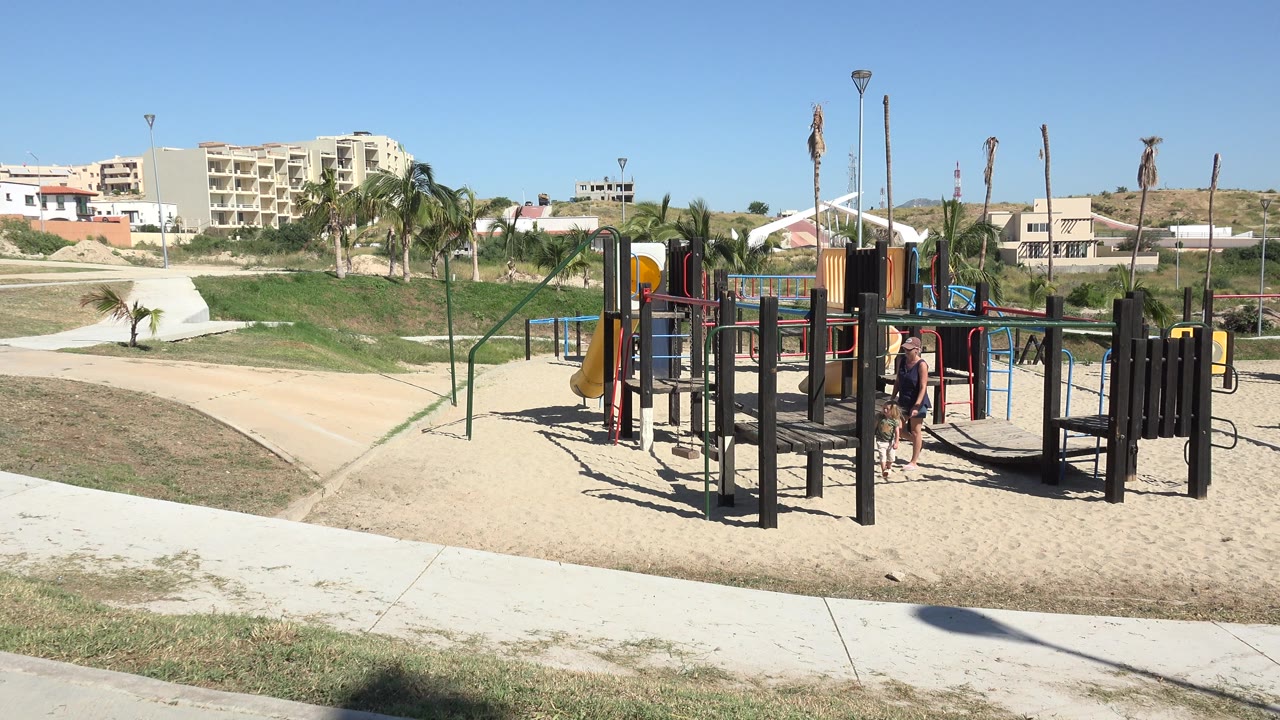 Wide playground view with an adult and child near play equipment.