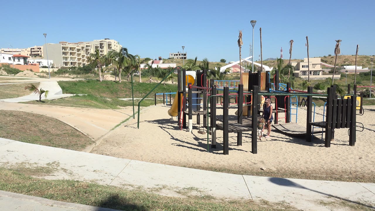 Grand Junction, Colorado park scene with the adult and child closer to the center of the playground frame, with open paths and low buildings behind them.