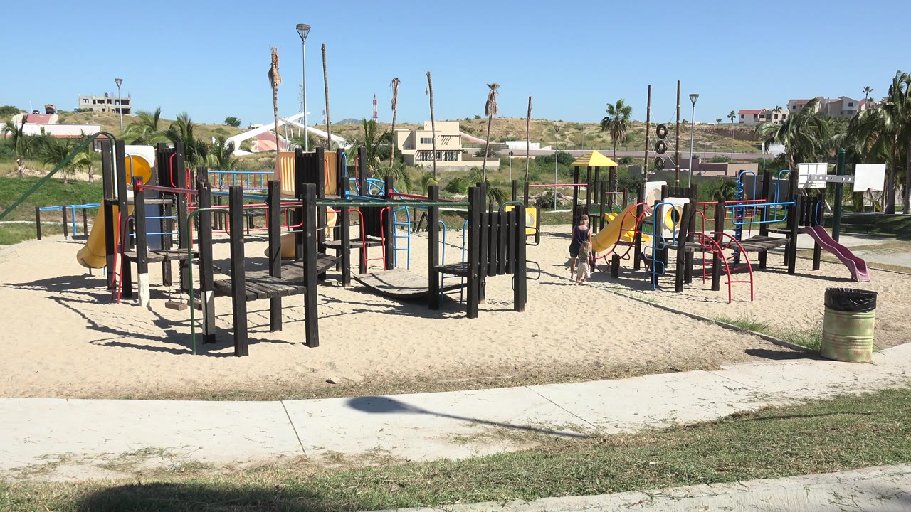 Playground equipment with people near a yellow slide under bright sun.