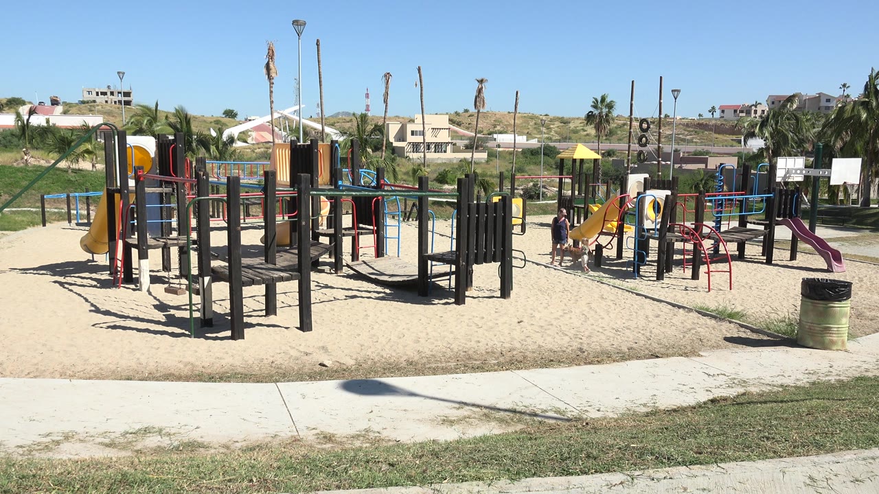 Wide sunny playground with children near slides and climbing structures.