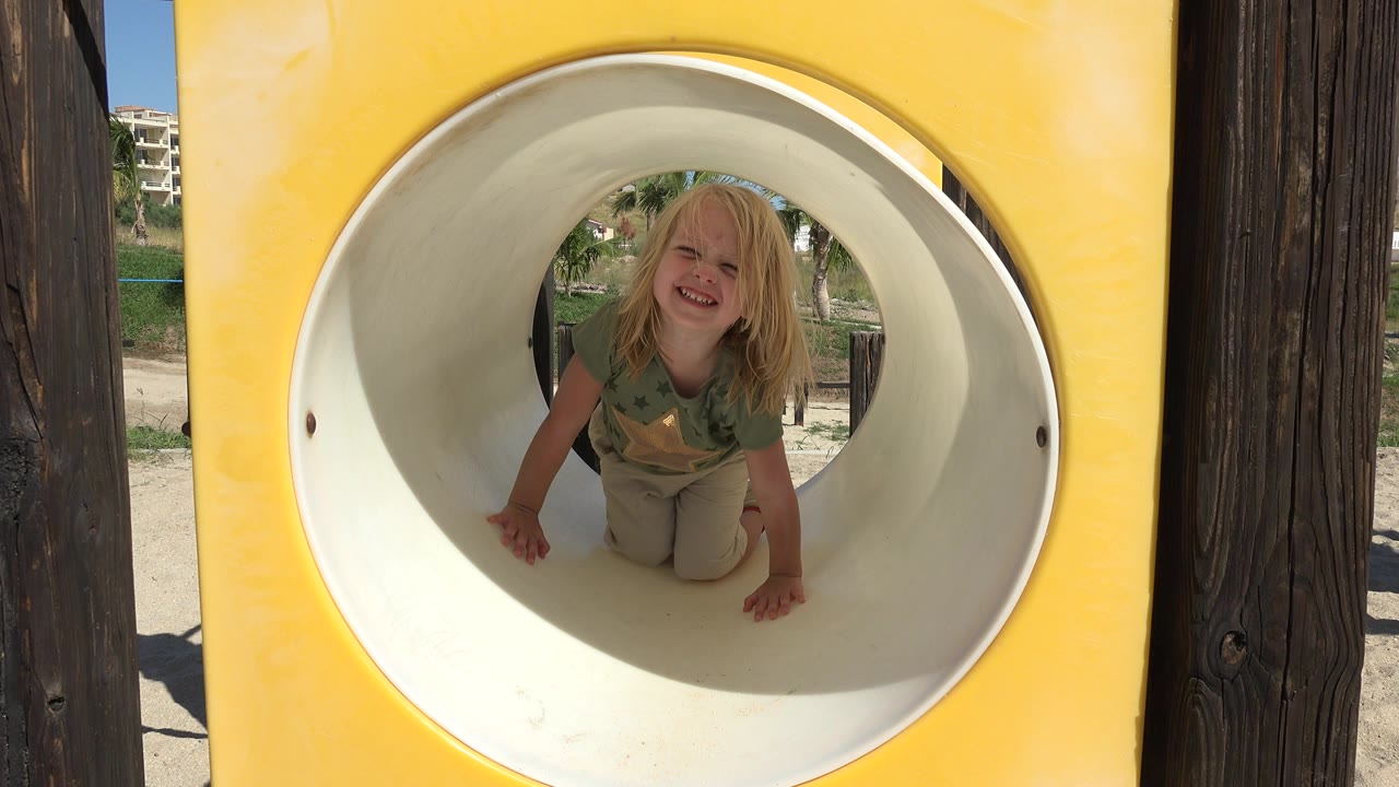 At 0:00, a blond child smiles toward the camera from inside a white playground tube slide in Grand Junction, Colorado.
