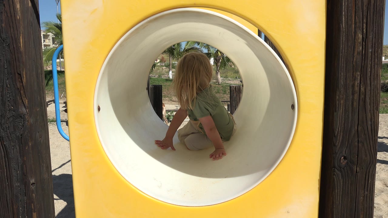 Child seated inside a white playground tube framed by a yellow panel.
