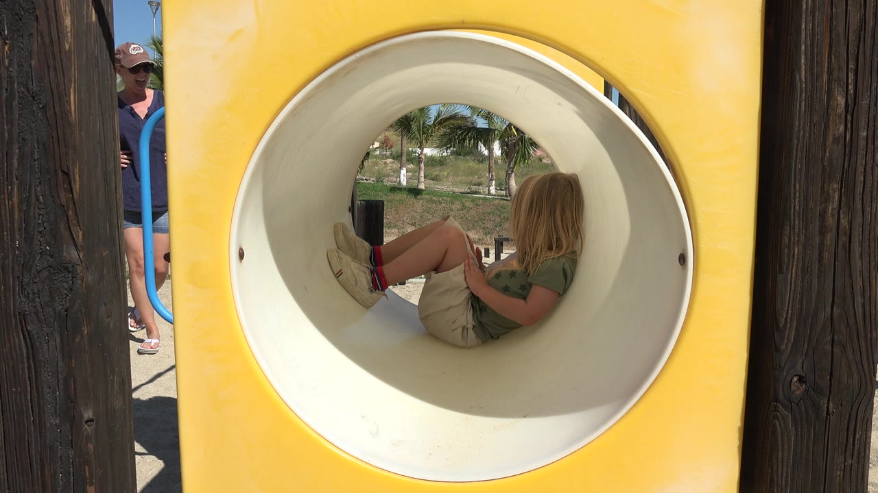 Blond child sitting inside a circular playground tube.