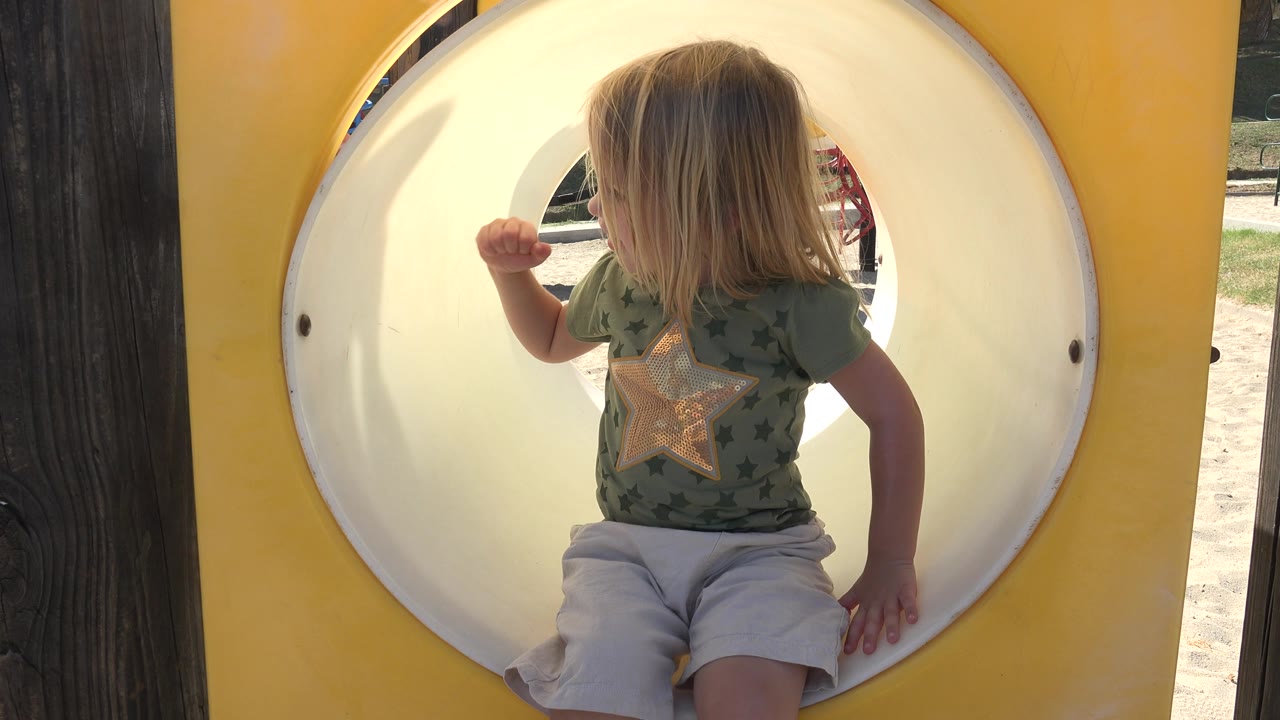 The child remains seated in the yellow tube slide opening in Grand Junction, Colorado, with her hair covering most of her face and her right arm bent near the slide wall.