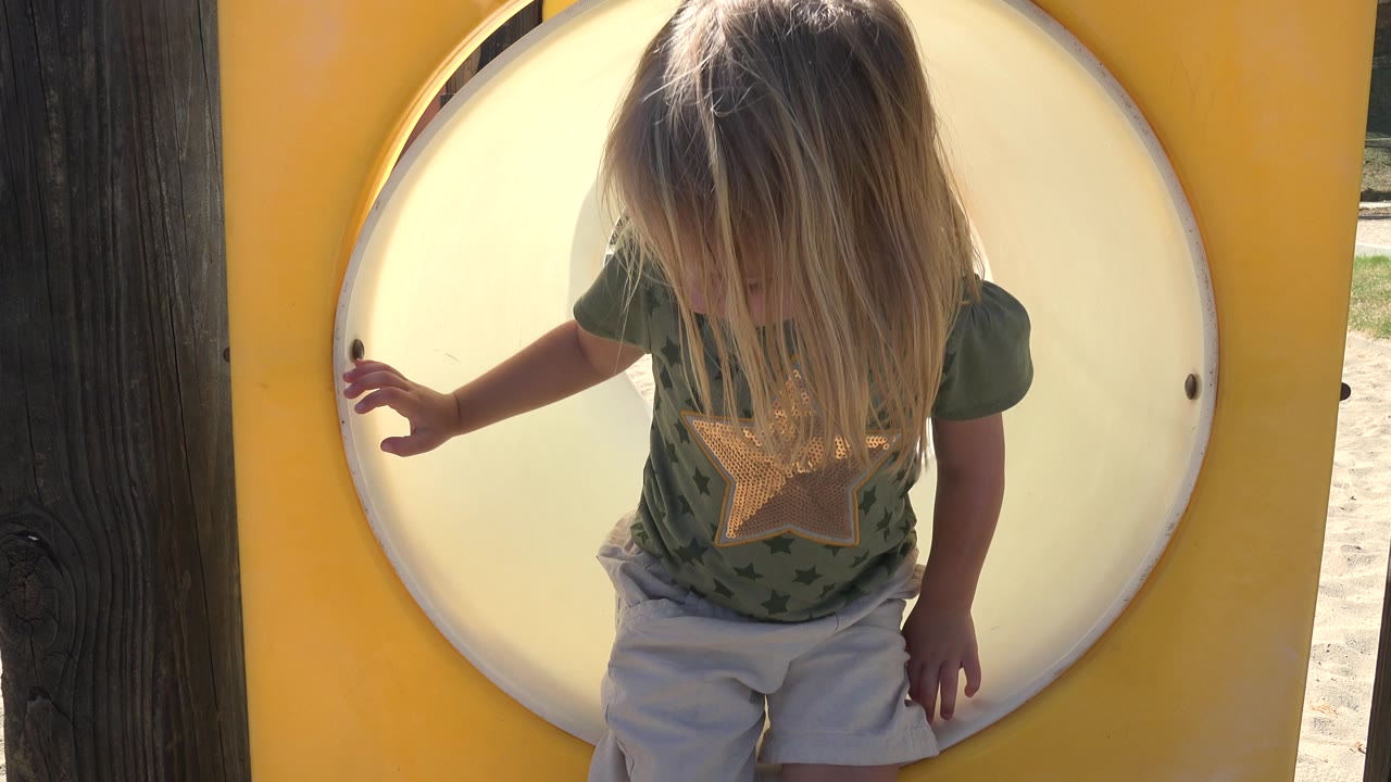Young child standing in front of a circular playground tunnel.