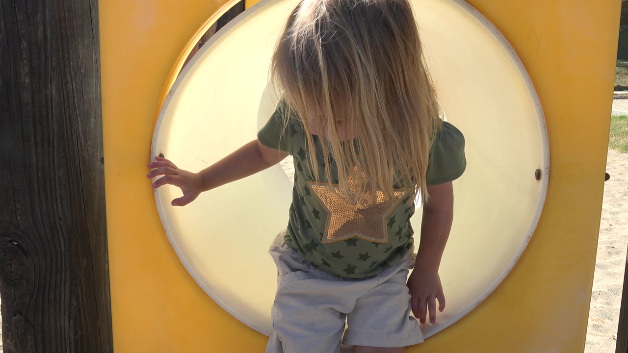 The child remains at the Grand Junction playground tunnel with one hand near the rim, hair hanging forward as bright light fills the pale circular opening.