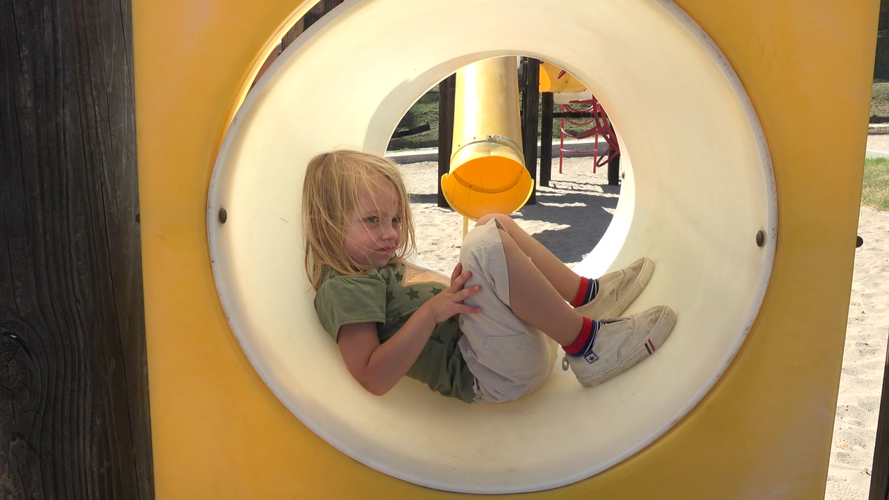 Young girl curled inside a white playground tunnel.
