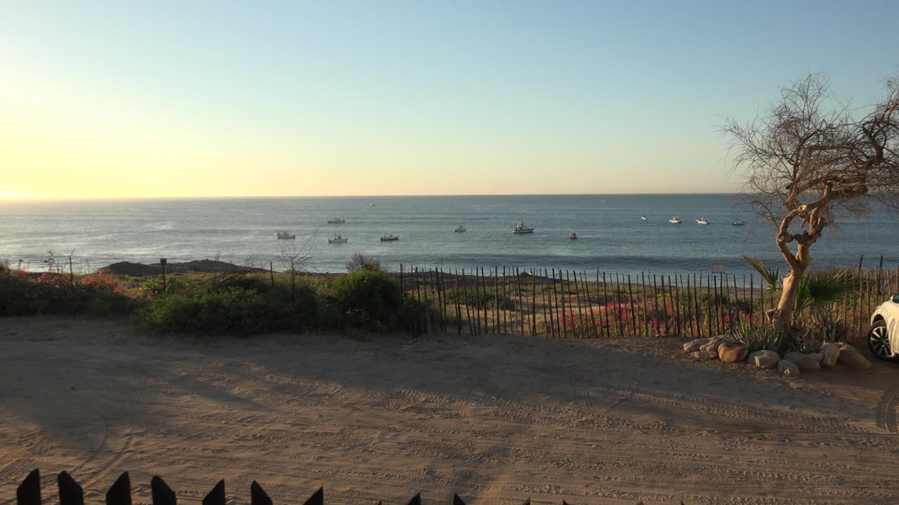 Grand Junction, Colorado collection frame with the sea horizon centered, small boats spread across the water, foreground sand and fence in shadow, and no visible people at 0:01.