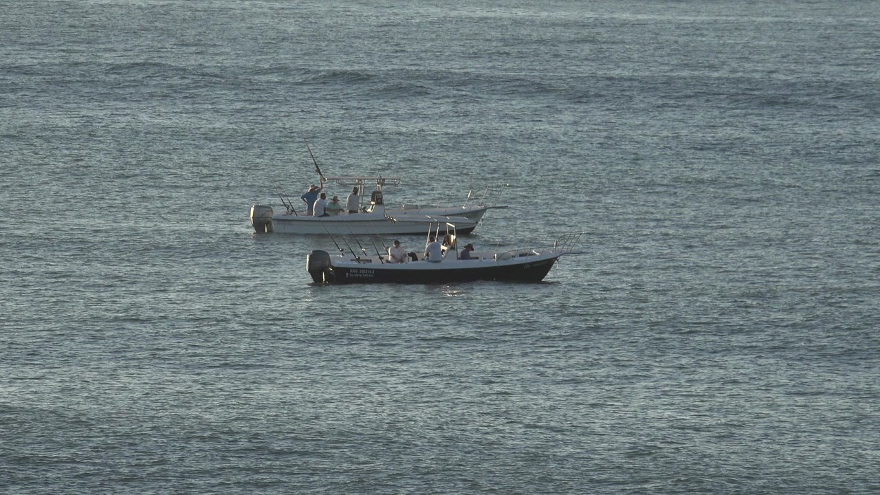 Two grey boats float close together on rippled water in Grand Junction, Colorado, with small distant occupants visible aboard both boats.
