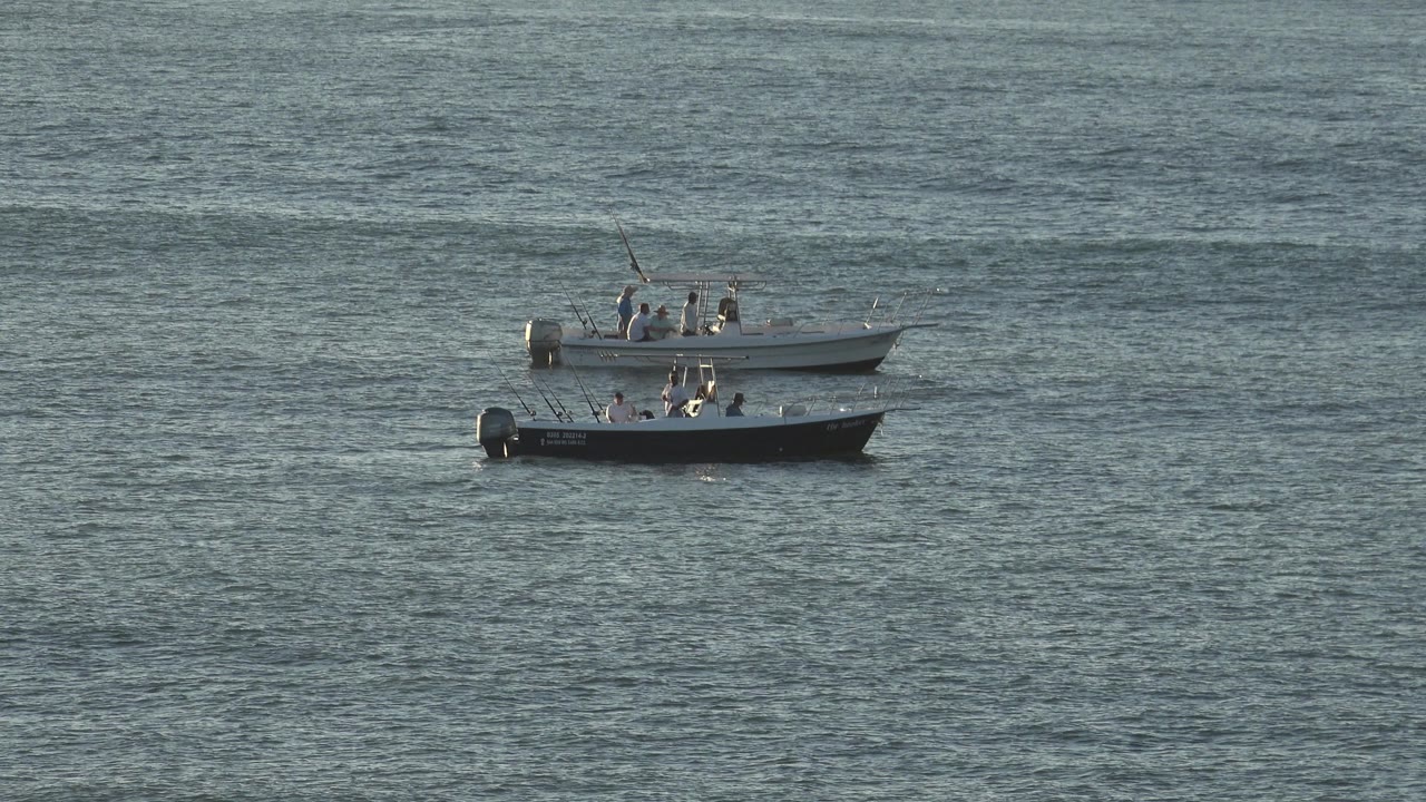 The dark blue boat and white boat remain close together on the river in Grand Junction, Colorado, with passengers visible as small figures.