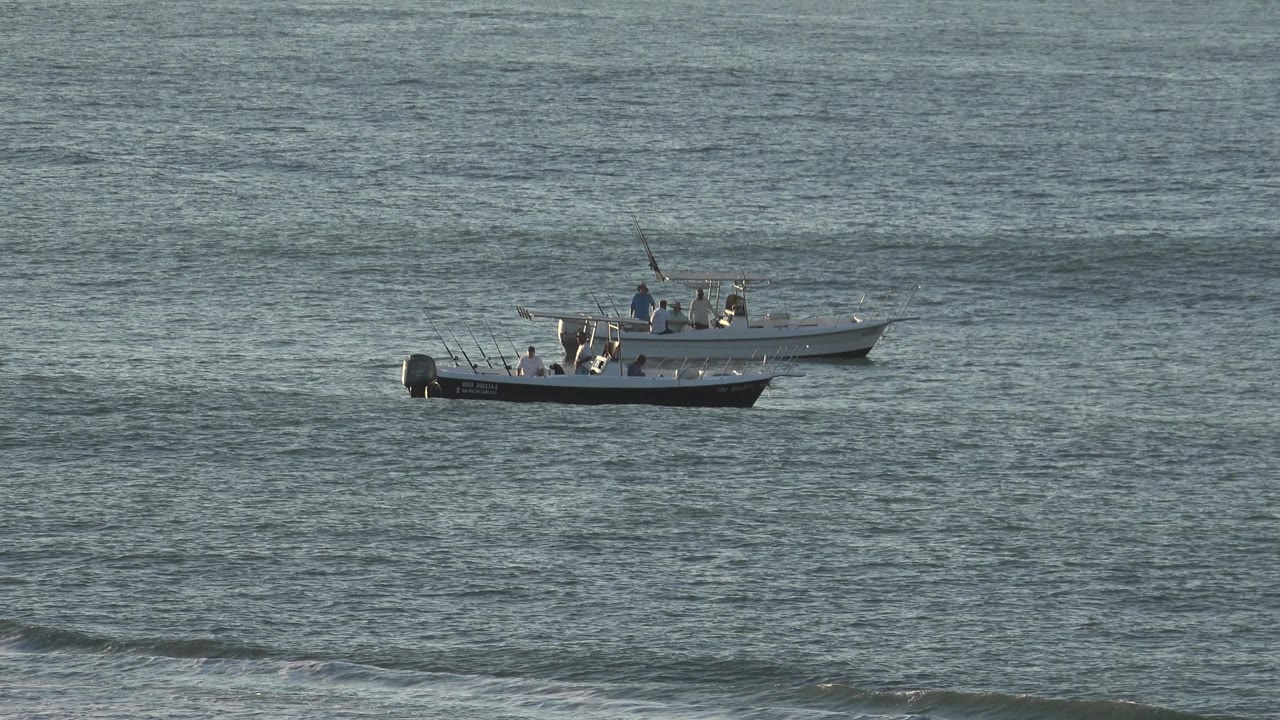 Fishing boat on open water with rods raised and people aboard.
