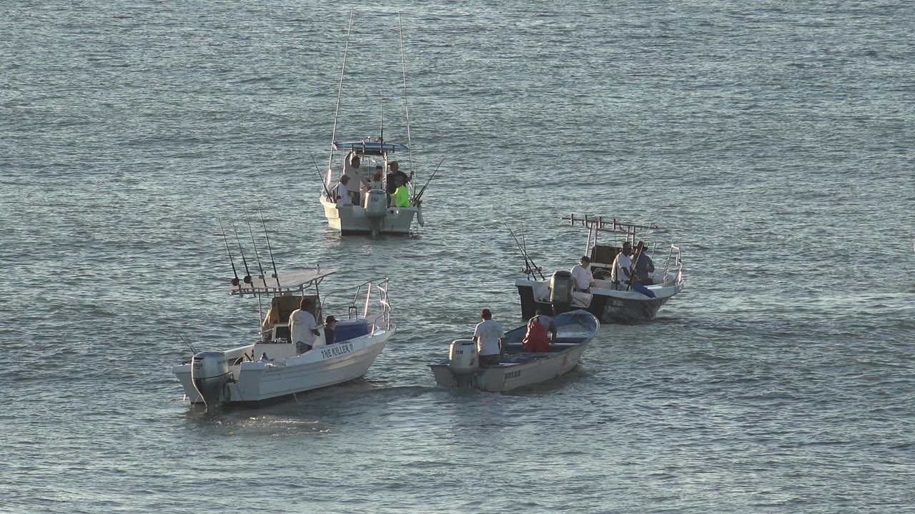 The boats remain grouped on the water in Grand Junction Colorado, with seated and standing people visible and fishing rods angled above the hulls.