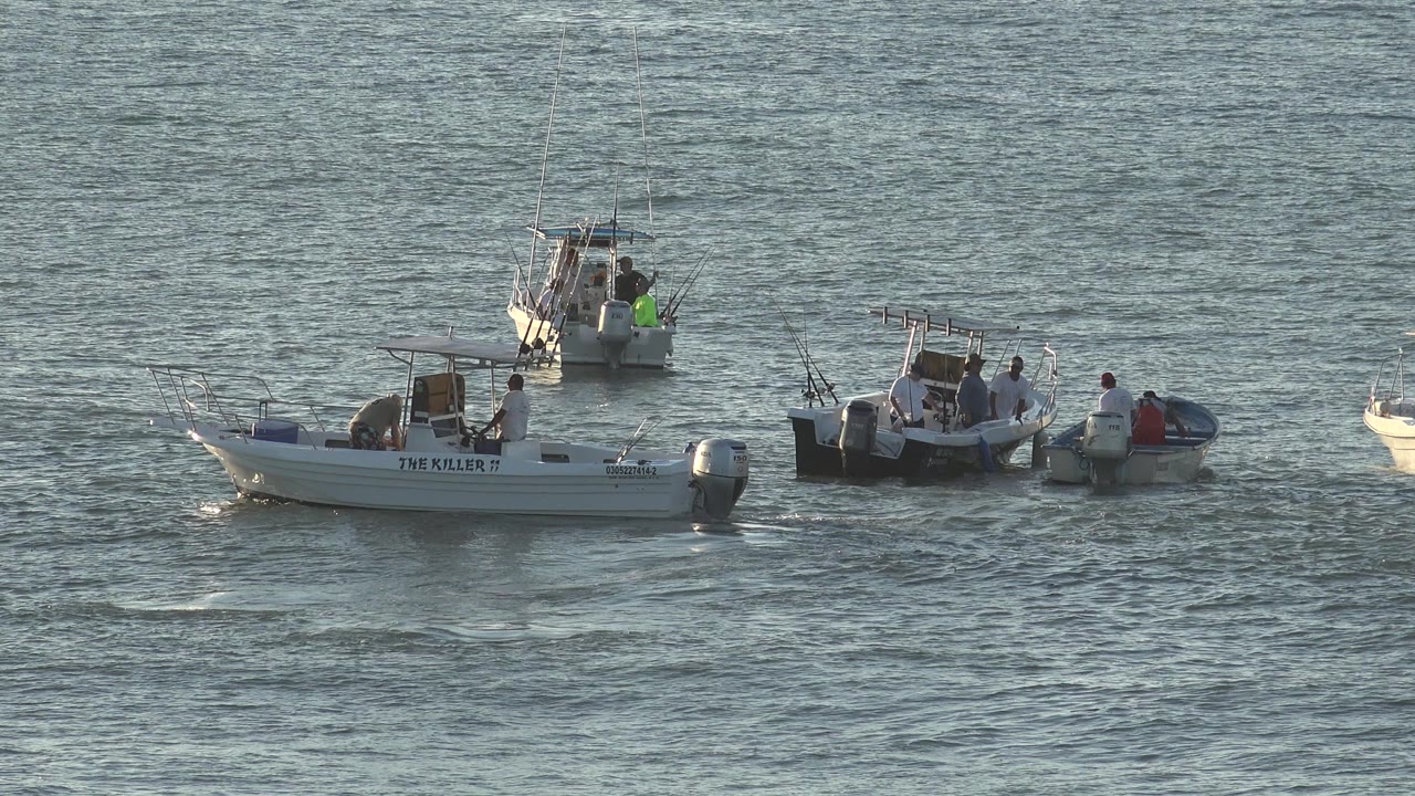 In Grand Junction, Colorado footage, three small boats are spread across blue-gray water, with people gathered around the center boats and a white boat name visible on the left hull.