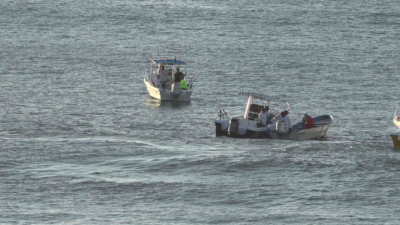 Two small fishing boats on rippled water with people aboard.