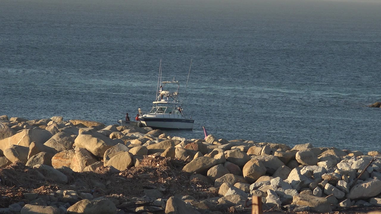 White yacht near shoreline rocks with open water behind it.