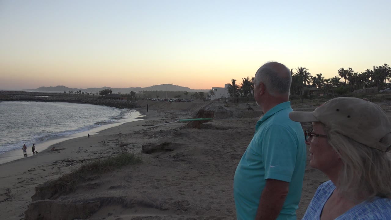 Older man and woman stand beside a beach at dusk.