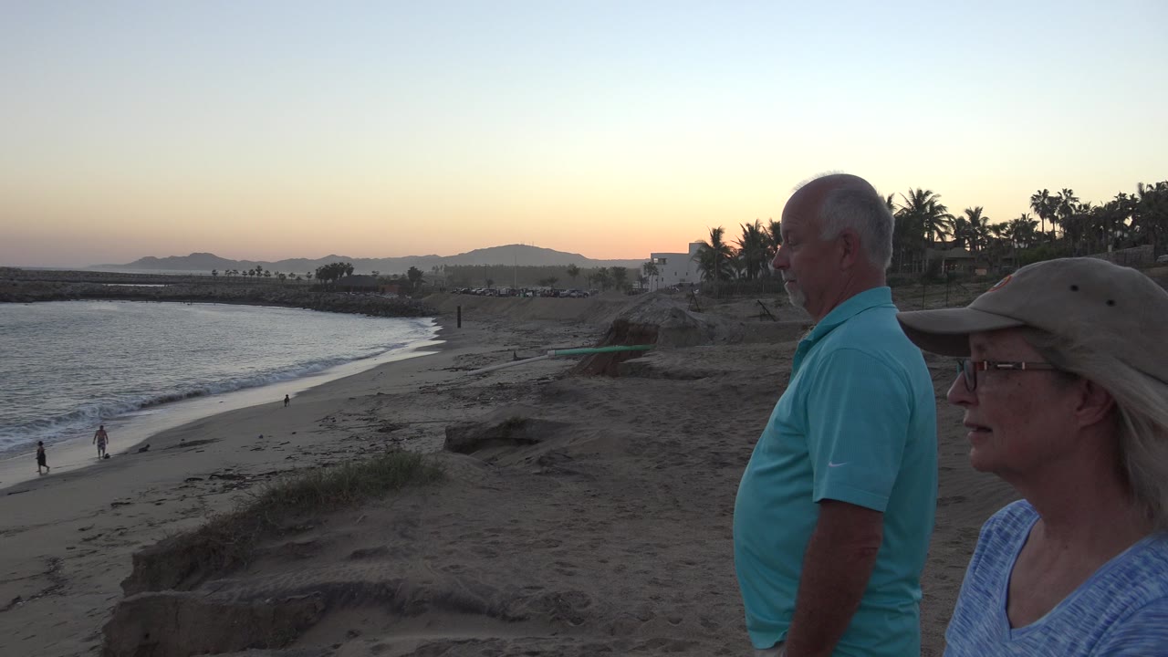 Older couple in foreground overlooking a beach at dusk.