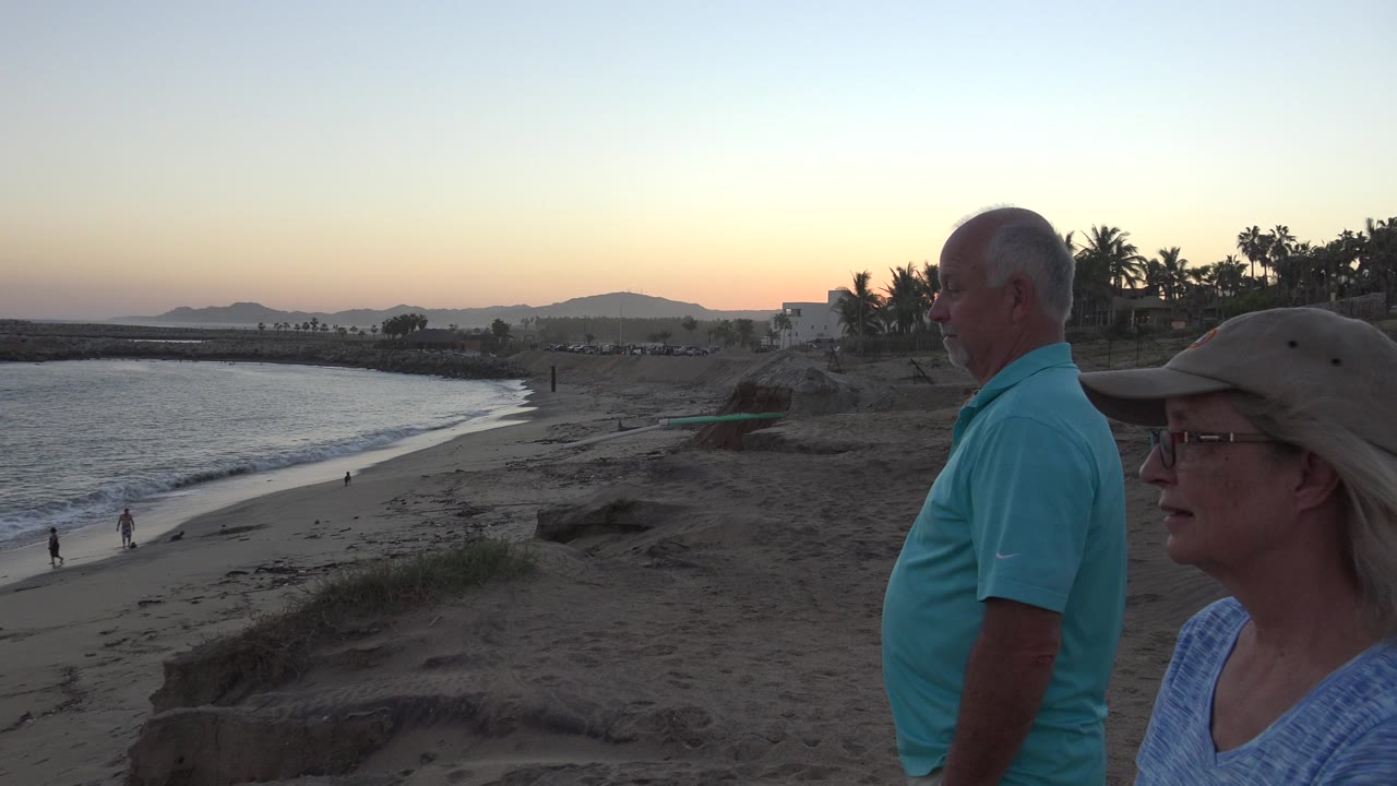 Older man and woman remain at frame right while the beach, low surf, rocky point, palm trees, and fading sunset color fill the Grand Junction, Colorado 2017 frame.