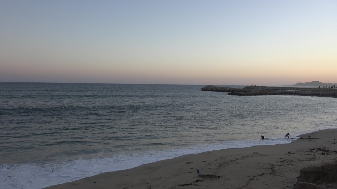 Wide beach and ocean view with small people near the surf.