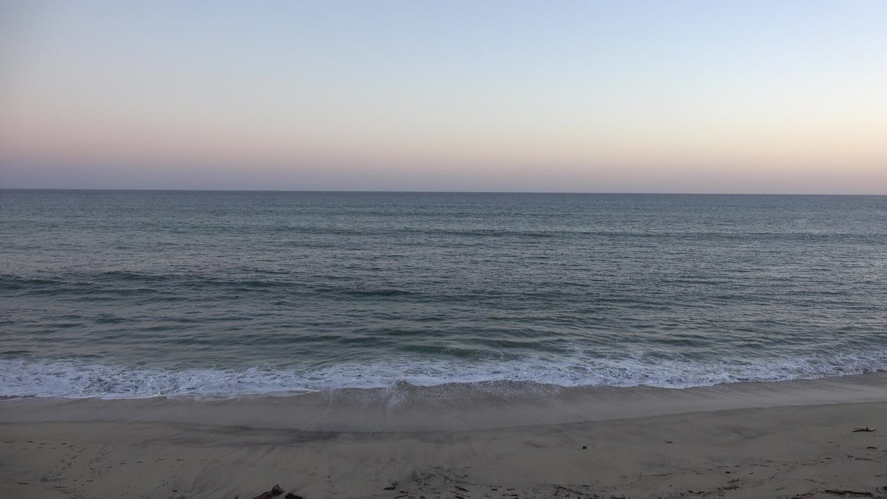 Opening frame of the Grand Junction, Colorado beach clip showing sand, low surf, a flat ocean horizon, and no visible people.