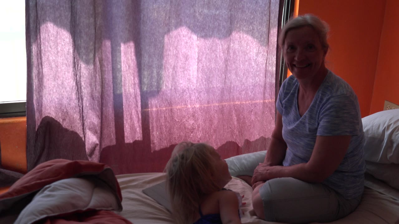 Woman sitting on a bed beside a child near purple curtains.