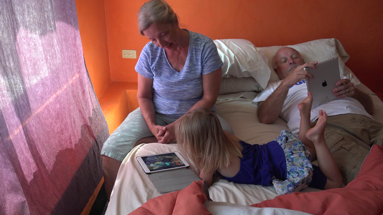 Family on a bed using tablets in an orange bedroom.