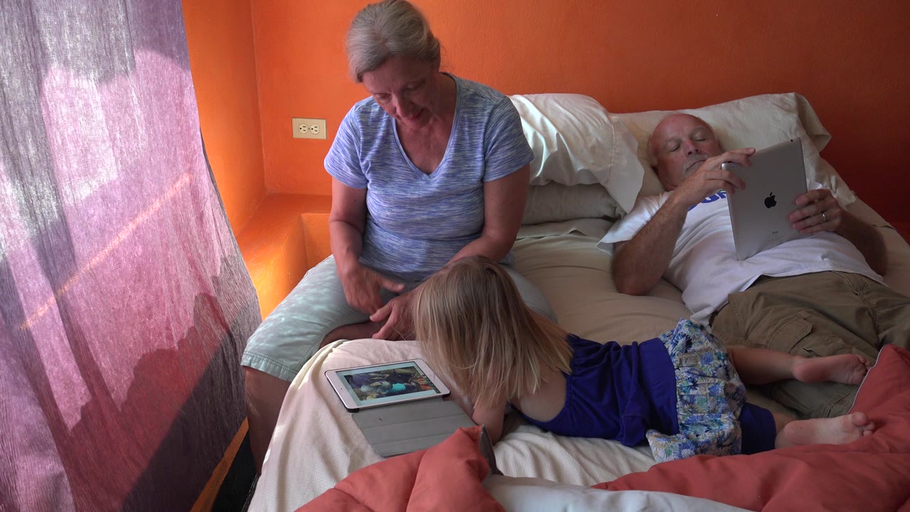 Older woman and child on bed while older man uses a tablet