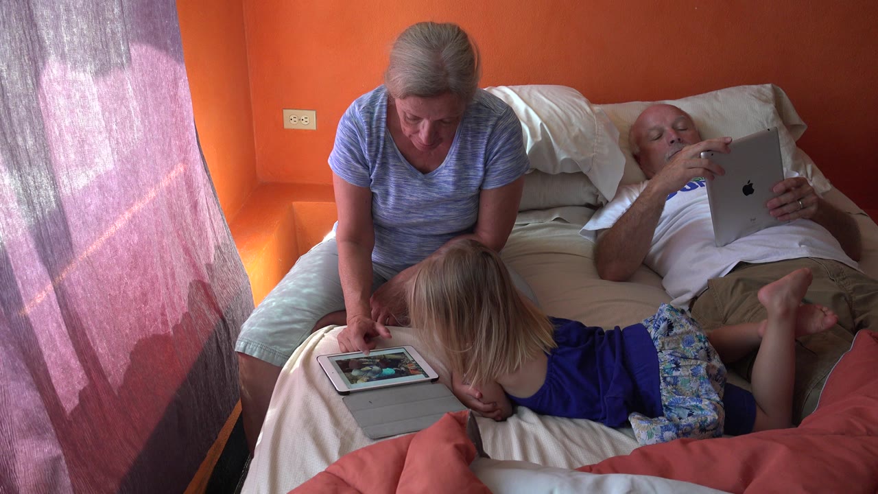 Woman and child on a bed while an older man holds an iPad.