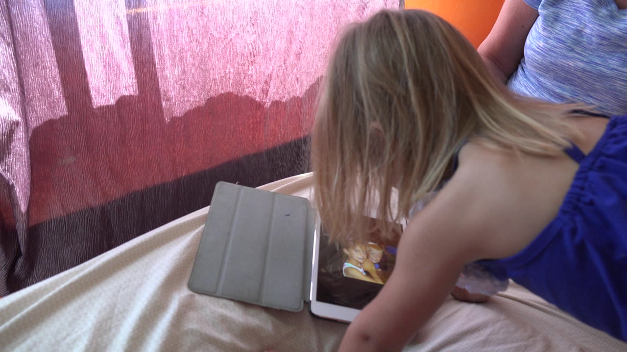At 0:01 in Grand Junction, Colorado, the child remains bent toward the tablet screen, with hair covering much of the face and the adult cropped at the shoulders and torso.
