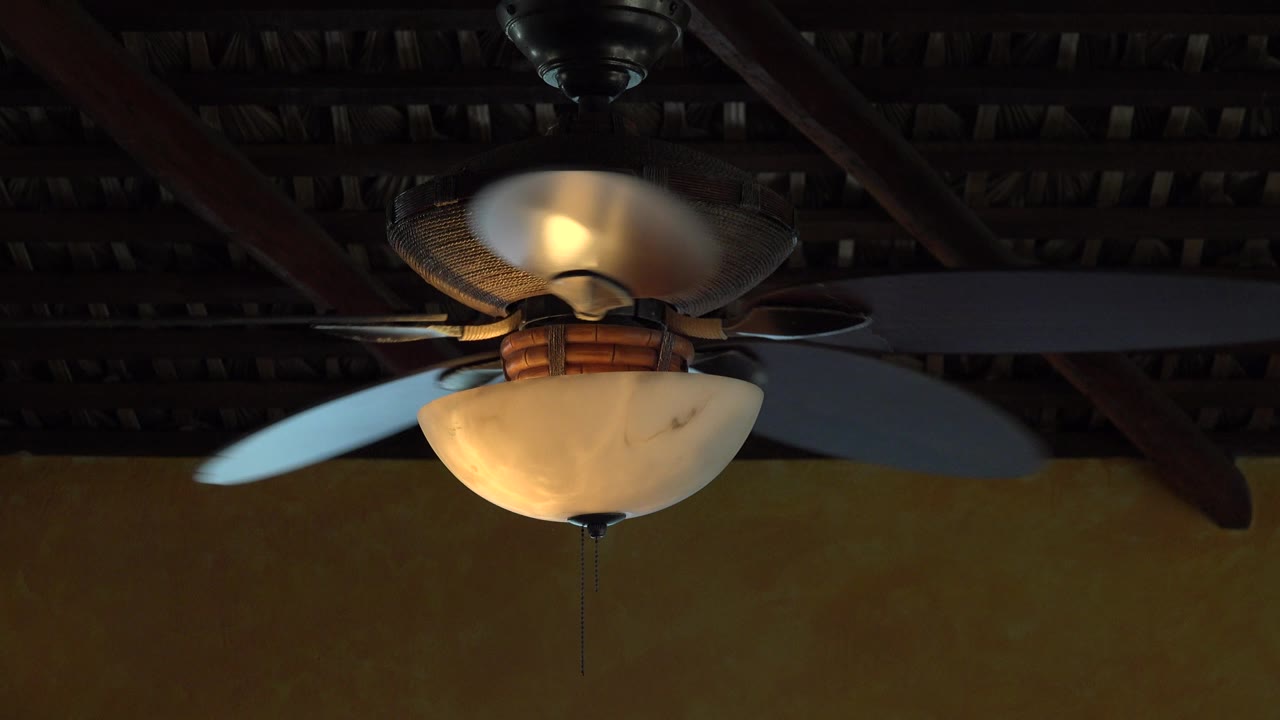 White ceiling fan with glowing lamp under a dark ceiling