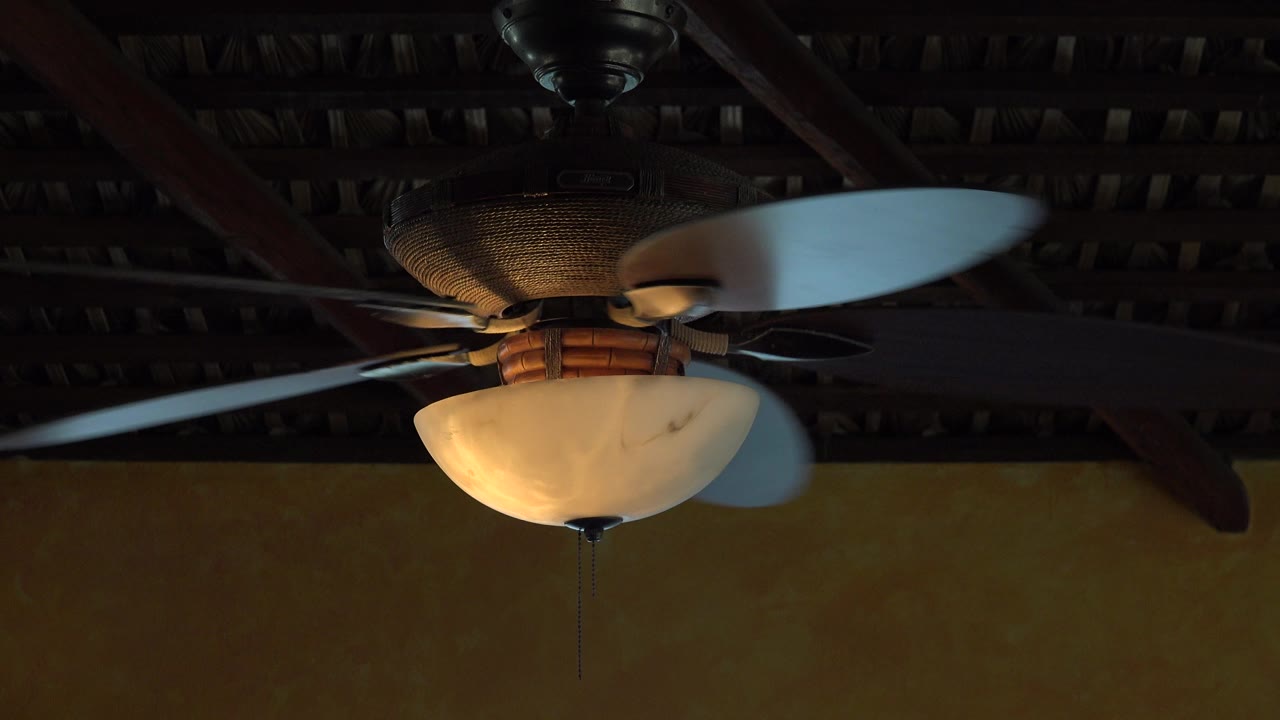 Spinning ceiling fan with warm light under a dark exposed ceiling.